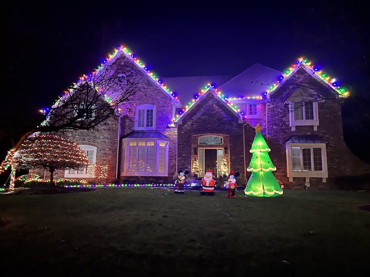 A two-story brick home outlined in multicolor roofline lights with an inflatable Christmas tree, Santa and Mickey figures on the lawn at night.