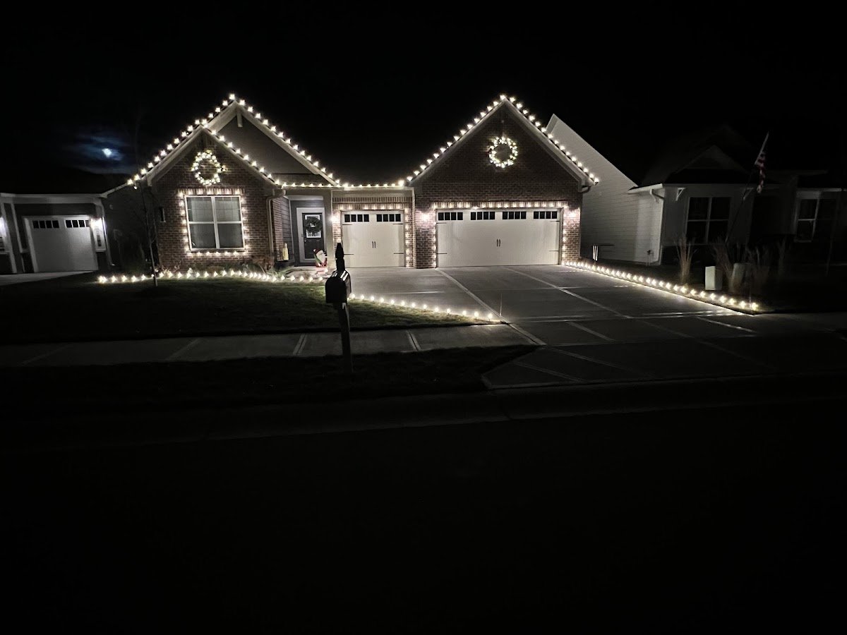 A single-story brick home outlined in warm white C9 bulbs with wreaths on the gables and warm white pathway lights lining the lawn and driveway at night.